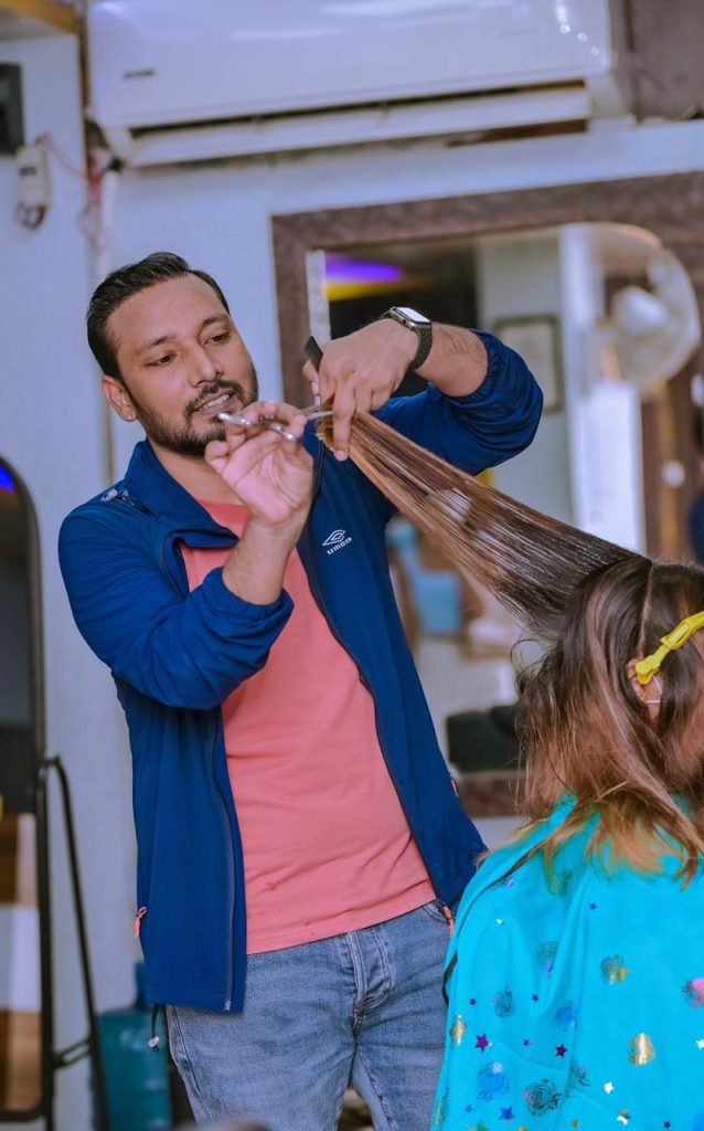 a man in blue outter wear cutting a ladies hair
