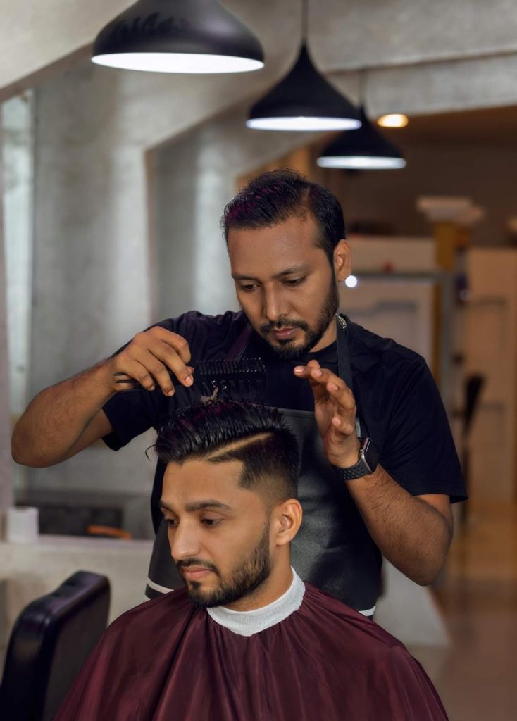 A male hair stylist wearing a black tshirt stylig a man's hair.