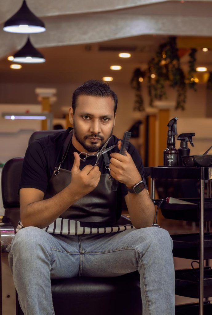 man in black tshirt holding scissor sitting in a chair